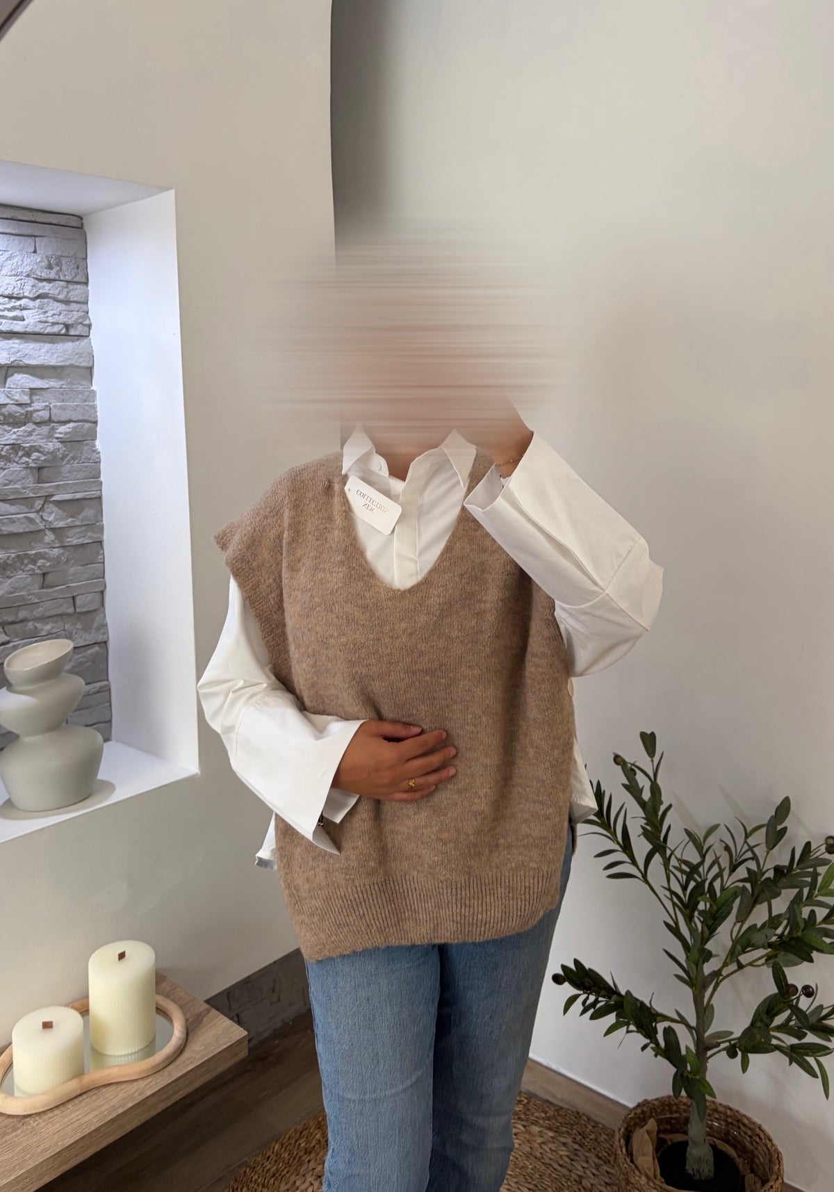 Pull sans manches beige à boutons dorés porté sur une chemise blanche