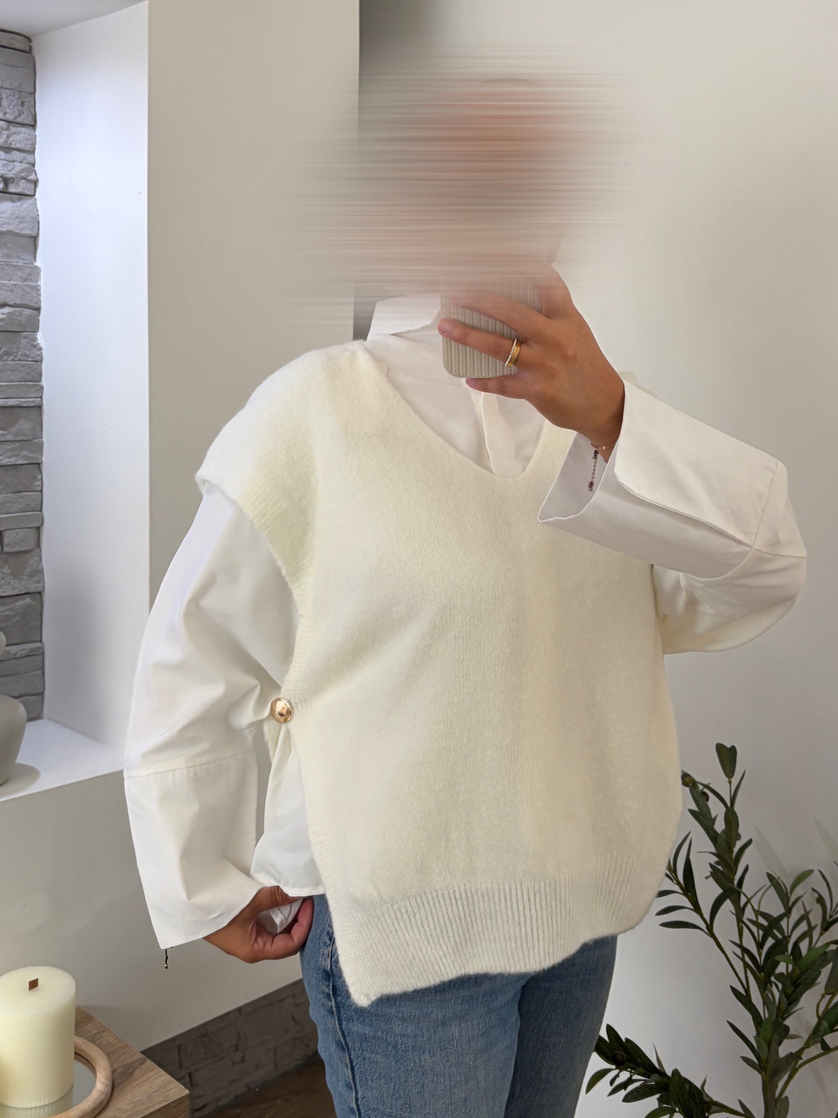 Pull sans manches blanc à boutons dorés porté sur une chemise blanche